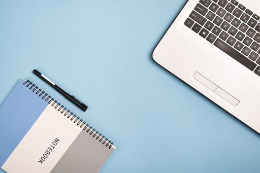 A top view of an open laptop, a notepad, and a pen on a blue background