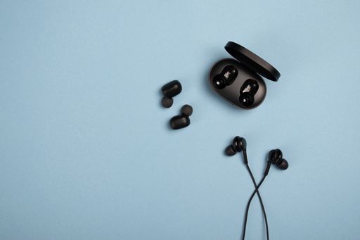 A top view of black earphones and wireless earphones with a case on a blue background