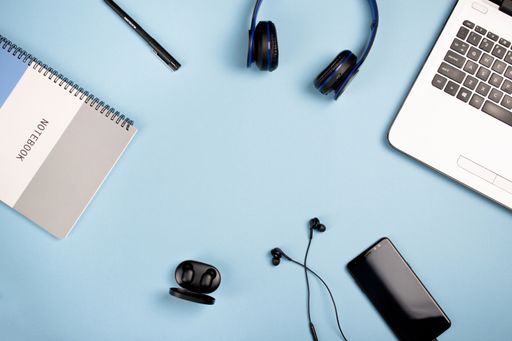 A top view of a notebook, notepad, headphones, earphones, smartphone, pen on a blue background