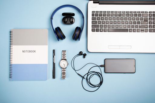 A top view of a notebook, notepad, headphones, earphones, smartphone, pen, watch on blue background