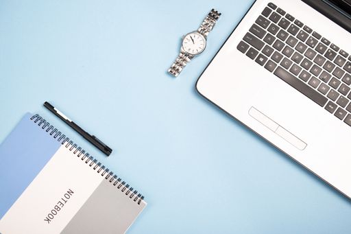 A top view of an open notebook, a notepad, a pen, and a watch on a blue background
