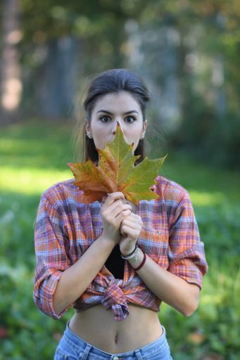 A vertical shot of a young caucasian female posing in a park with a leaf