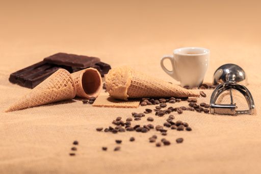 Appetizing almond ice cream cone surrounded by out of focus coffee beans, coffee cup and chocolate chunks: Selective focus. Ice cream concept.