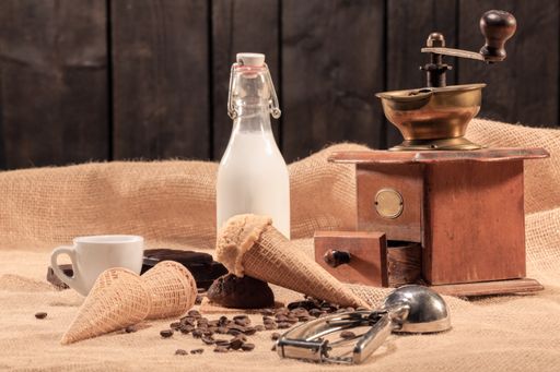 Tempting ice cream cone with coffee beans, a bottle of milk, a coffee cup and a classic coffee mill. Selective focus. Ice cream and sweets concept.