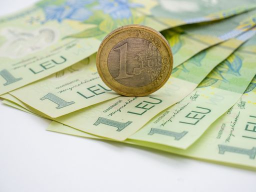 A one euro coin put on Romanian banknotes of one leu on a white table