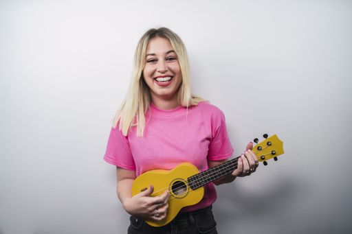 A young cheerful Caucasian female from Spain playing ukulele against a white wall