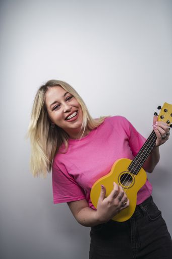 A young cheerful Caucasian female from Spain playing ukulele against a white wall
