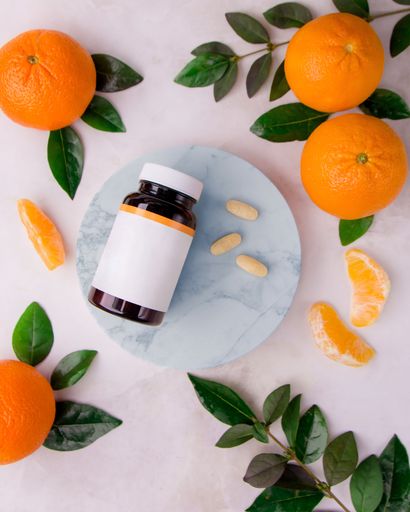 A vitamin jar with orange pills surrounded by fresh oranges on white background with copyspace
