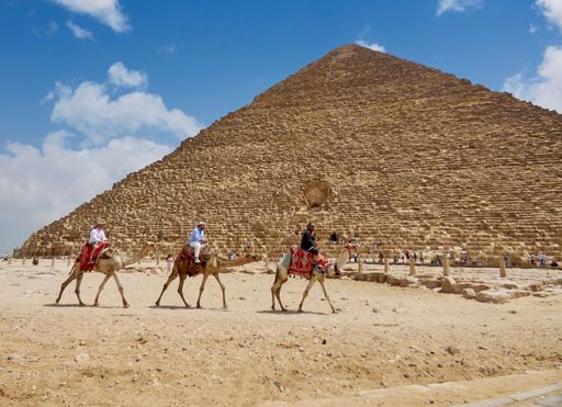 A group of tourists riding camels in front of an iconic Egyptian pyramid.