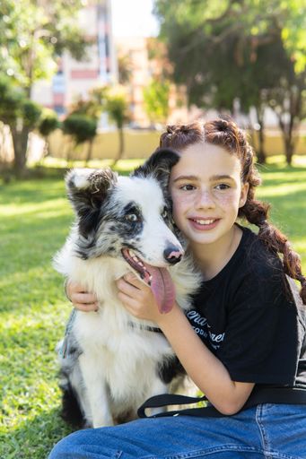 A vertical shot of a girl and a dog sitting on the grass in a park