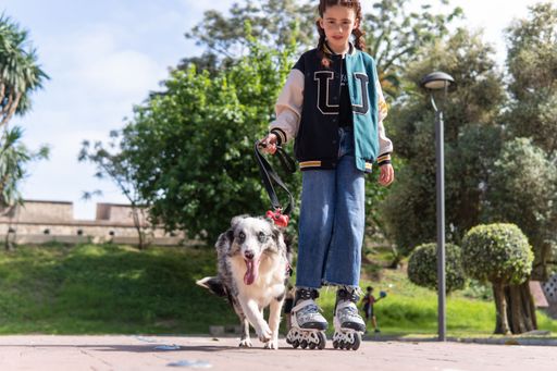 A red-haired girl in roller skates walking a dog in the park