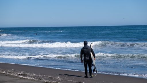 man looking at the sea with his surfboard and wetsuit, a beach in Chile sunny day small waves