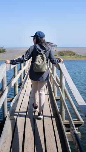 woman walking towards the beach, crossing a bridge on a sunny day in the beach of Chile vertical photo