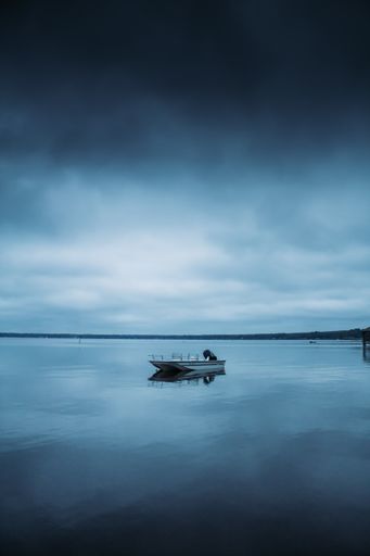A sleek sailboat is sailing on the calm waters of a tranquil lake at dusk, with a beautiful pastel sky