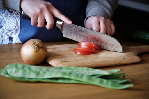 A close-up of a person cutting tomatoes into thin slices on a countertop surface