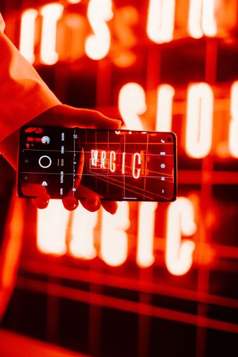 A woman's hand holding a phone and taking a picture of a wall illuminated by red light.