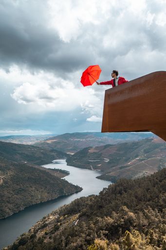 A man on the viewpoint holding a red umbrella against the background of a cloudy sky. Portugal, Douro.