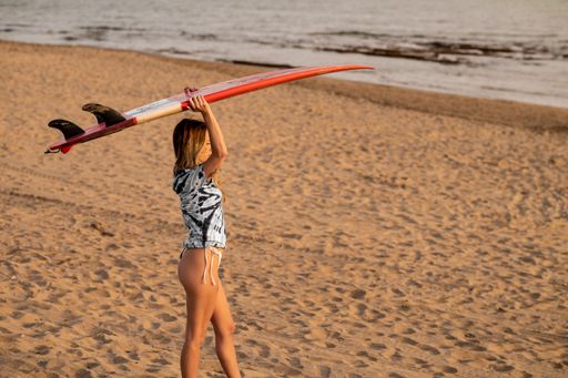 A young blonde female surfer walking at the beach with her surfing board