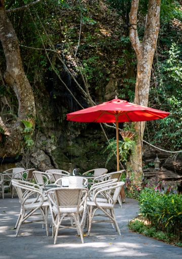 A tranquil outdoor setting featuring an array of tables and chairs sheltered by a large red umbrella