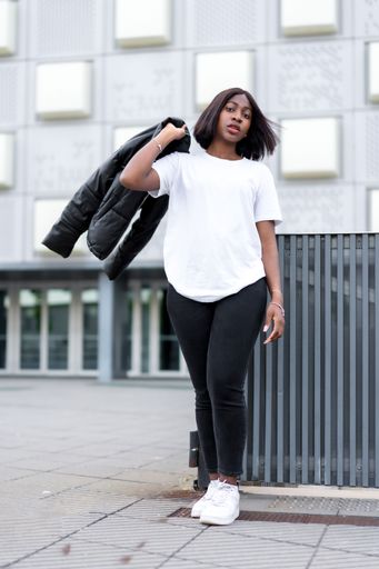 An attractive black female posing confidently in a casual outfit holding a black coat