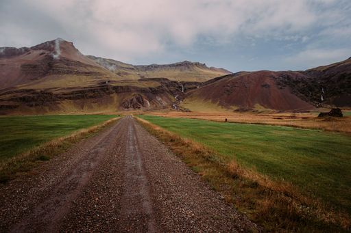 Icelandic rustic landscape featuring a dirt road running through lush green grass with majestic mountains in the background