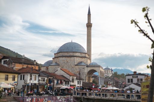 An old urban cityscape featuring a large crowd of people walking past the Sinan Pasha Mosque