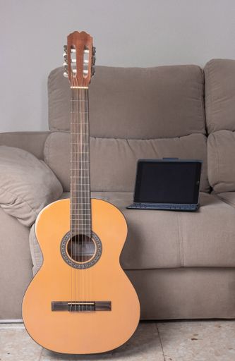 A vertical shot of a guitar and a tablet on the sofa of a house. Concept of learning to play guitar from home