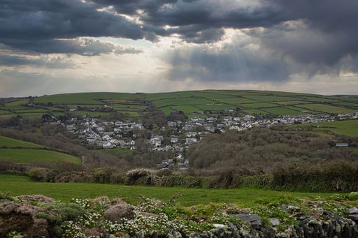 A scenic view of a lush green valley and the town of Tintagel, Cornwall under a dramatic sky