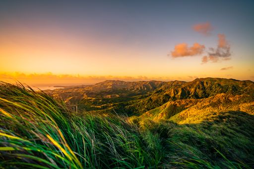 An idyllic landscape featuring a beautiful sunset over a mountain range, with lush grass and vibrant colors, Guam