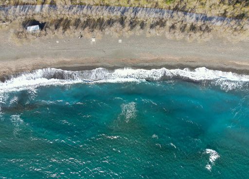 An aerial view of a sand beach with soft foamy waves washing against the shore