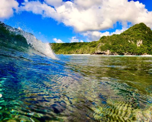 An ocean wave breaking with beach and cliff in background, Guam