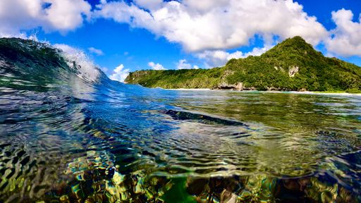 A majestic view of a calm beach in Guam with a foaming ocean wave crashing against the shoreline