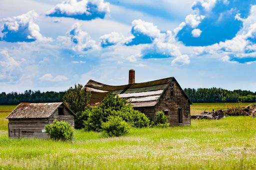 A small wooden farmhouse in the green meadow under the blue cloudy sky