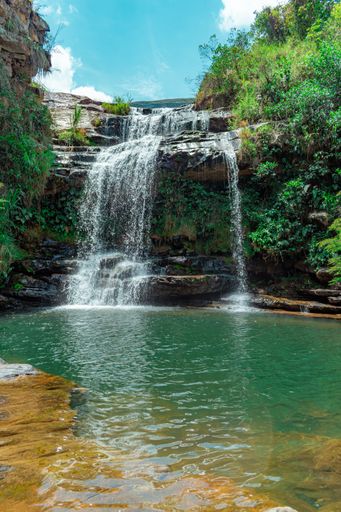 A beautiful vertical shot of a waterfall in a jungle with bright blue sky and greenery