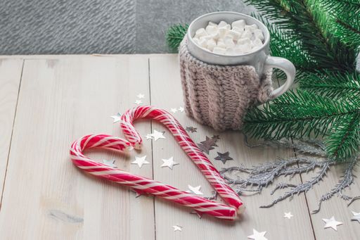 A mug of marshmallows and candy canes surrounded by Christmas decorations on a wooden table