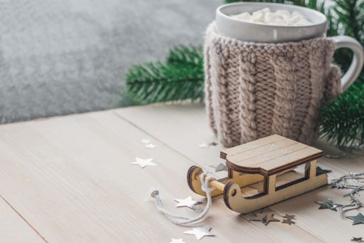 A closeup of a wooden sledge ornament with a mug of marshmallows on the wooden table