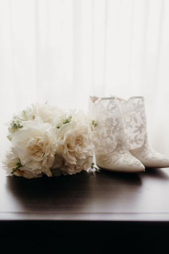 An arrangement of wedding bouquet and shoes on a table in front of a window