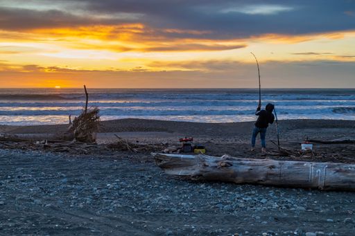 Otaki Beach, Wellington, New Zealand. May 2 2023. A man is drone fishing at sunset on the beach, it appears from the bend in the rod he has a fish on