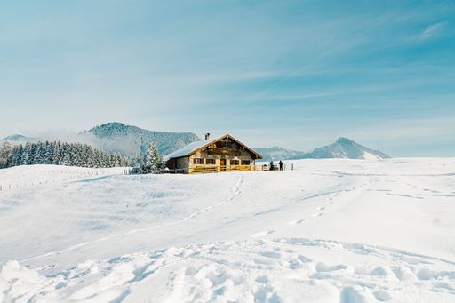 A scenic snow-covered landscape featuring a small log cabin in the distant background