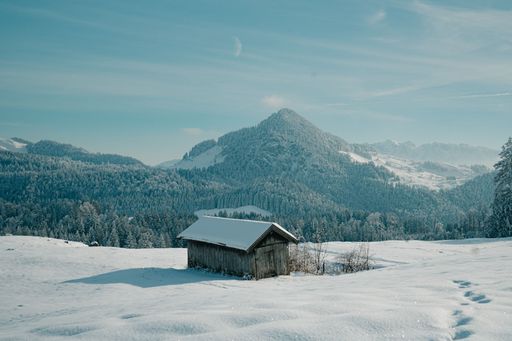 A scenic snow-covered landscape featuring a small log cabin in the distant background