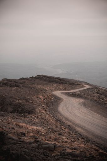 A winding dirt road leading up to a mountainous landscape of rolling hills.