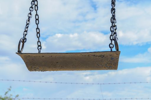 A low angle shot of a rusty old swing under a bright blue sky