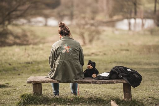 A back view of a woman sitting on a benc with a toy and a book next to her in the park
