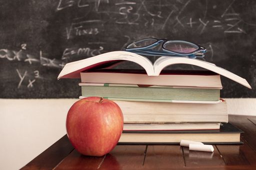 A close up shot of books, glasses and an apple in classroom