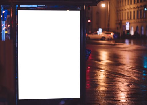 Bus stop with blank white space for your ad. Free copy space on illuminated bus stop during rainy night in urban european city.