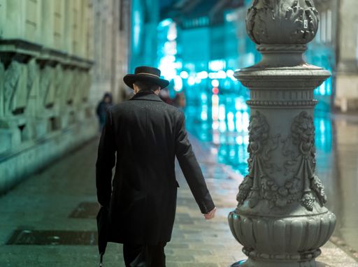 Elegant man walking in rainy night through german city of Munich. Wet ground is reflecting neon lights of the city.