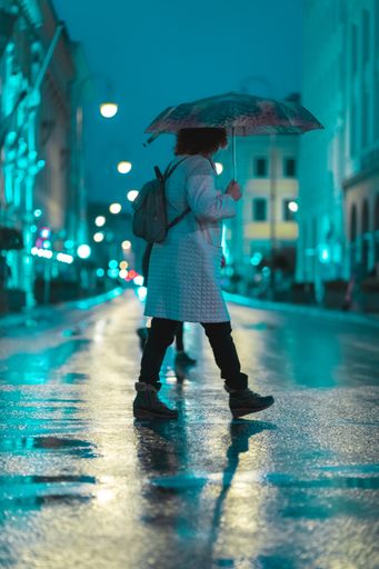 People crossing the street during a wet rainy night in Munich. Neon lights illuminating the scene. City traffic in the background.