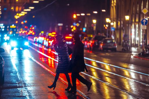 People crossing the street during a wet rainy night in Munich. Neon lights illuminating the scene. City traffic in the background.