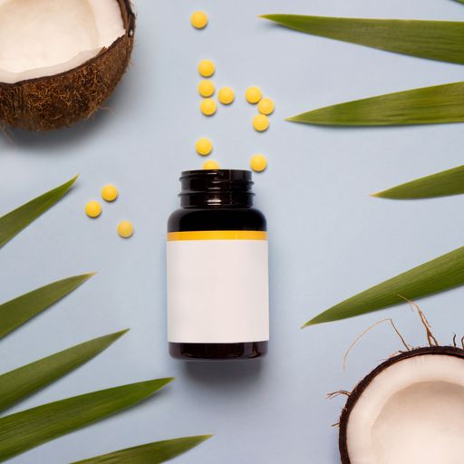 A bottle of vitamin-based supplement next to coconuts and green leaves on a white background