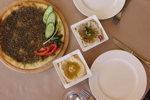 A table with a plate of pita bread topped with zaatar, hummus, and baba ghanouj
